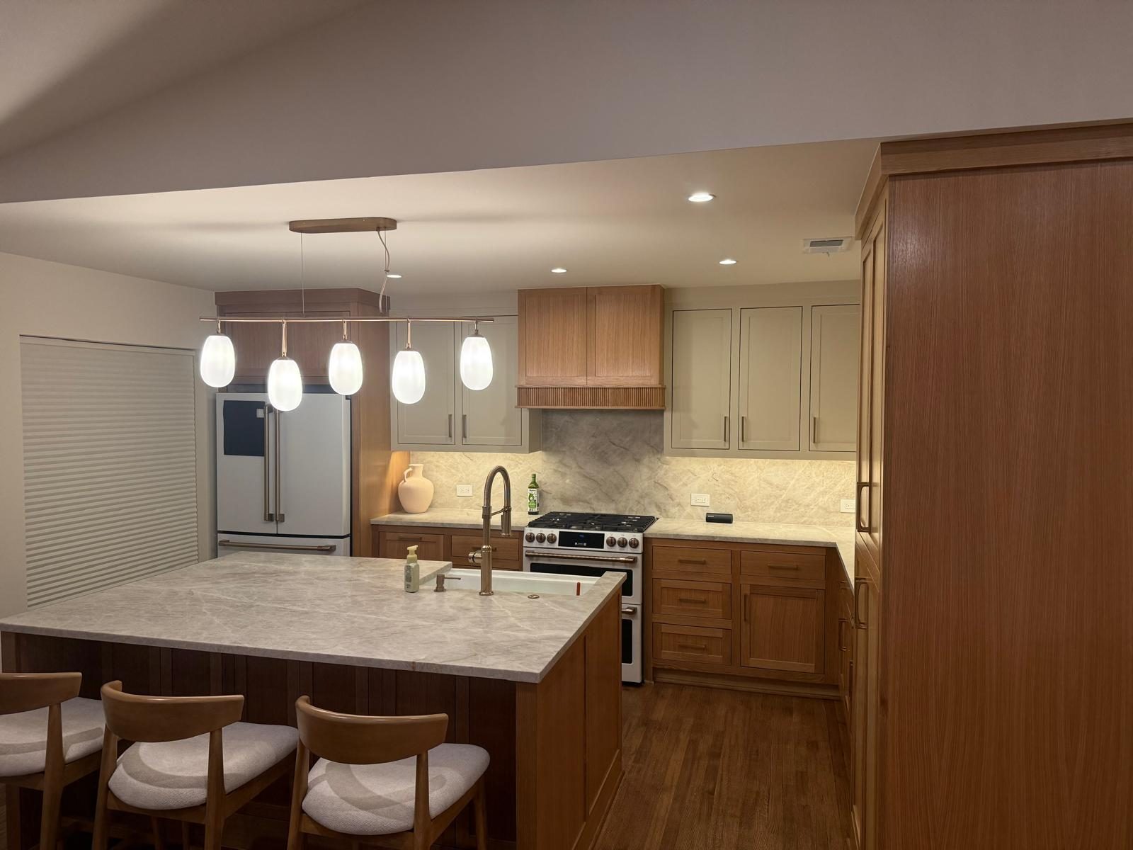 Kitchen with a marble-top island, wood cabinets, and pendant lights